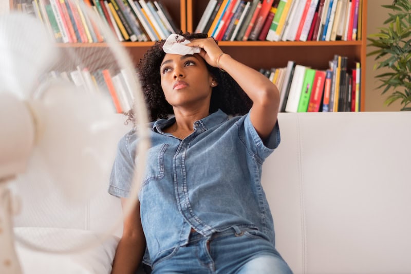 3 Tips to Prevent AC Breakdown During a Heat Wave. Woman sweating and trying to refresh at home.