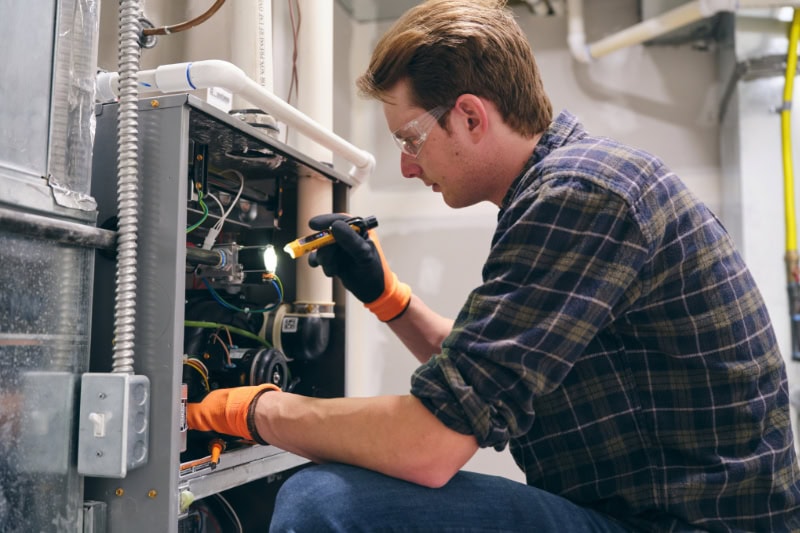 Schedule Your Annual Furnace Inspection Now. A repair man inspecting a furnace.