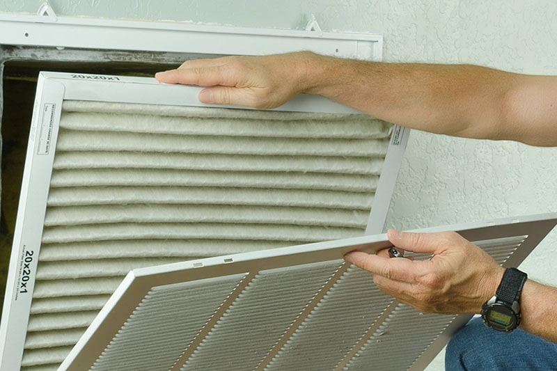 Everything You Need to Know About HVAC Filters. Professional repair service man or diy home owner removing a dirty air filter on a house air conditioner so he can replace it with a new clean one.